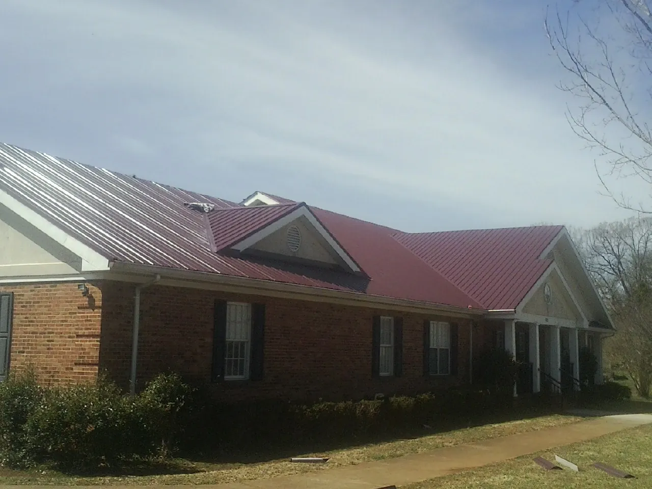 Red metal roof with gabled entries on a long brick building, from a Hail Damage Roof Repair job in Makoti