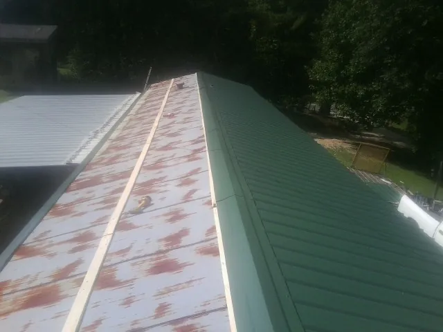 Old rusted panels beside newly installed green metal roofing — Wind Damage Roof Repair by Roofing Brothers in Makoti