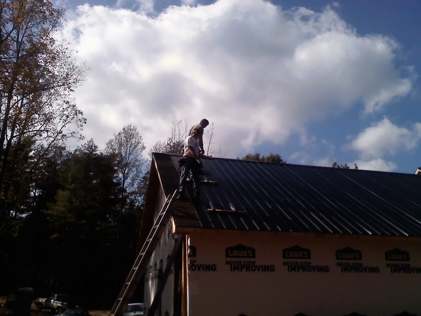 Roofer fastening dark metal panels high against a cloudy sky, from a Roof Inspection job in Makoti
