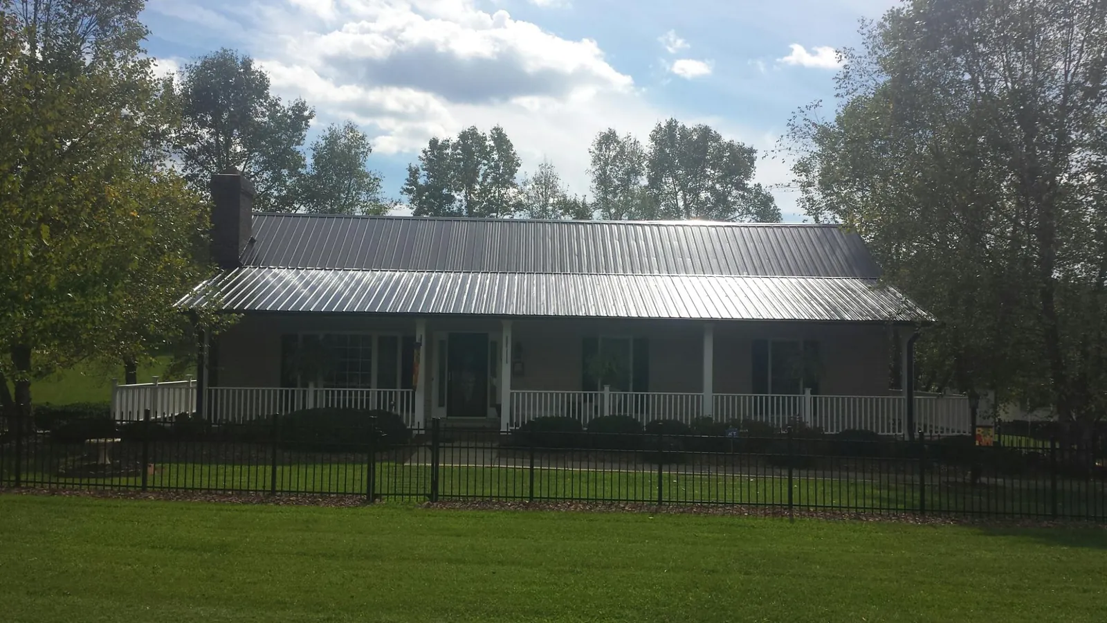 Gray metal roof on a brick ranch with a full width front porch — Gutter Guard Installation work by our crew in Makoti